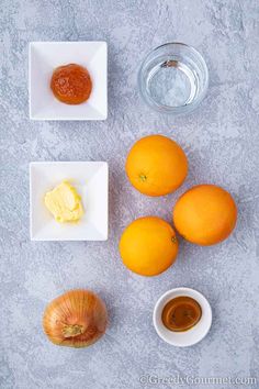 three oranges, two onions and some butter on a gray table with a bowl