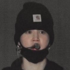 a woman wearing a black hat and scarf with a pacifier in her mouth,