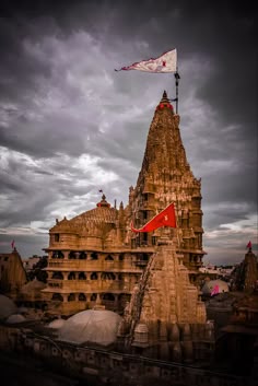 an old building with a flag on top and other buildings in the background under a cloudy sky