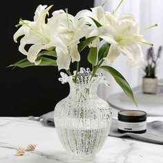 a glass vase with white flowers in it on a marble countertop next to other items