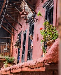 a person looking out the window of an old building with potted plants on it