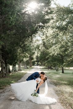 a bride and groom kissing on the side of a road in front of some trees