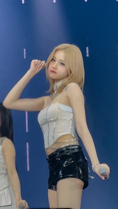 a woman standing on top of a stage next to another woman wearing short shorts and heels