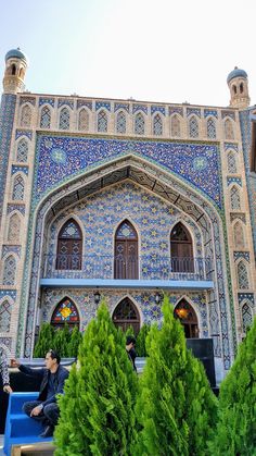 two people sitting on benches in front of a building with blue and white tilework
