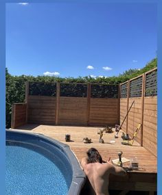 a man sitting on the edge of a swimming pool next to a wooden deck and fence