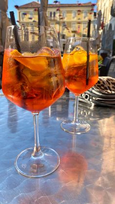 two wine glasses filled with drinks sitting on top of a metal table next to each other
