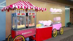 an old fashioned popcorn cart with pink and yellow cotton candy on the front, sitting next to a wall
