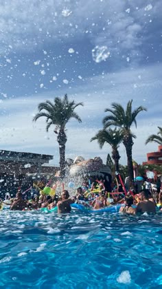 people are swimming in the pool with palm trees and blue sky behind them as water splashes