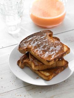 two pieces of french toast on a plate with syrup and orange juice in the background