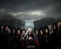 a group of women standing next to each other in front of a dark forest with birds flying overhead