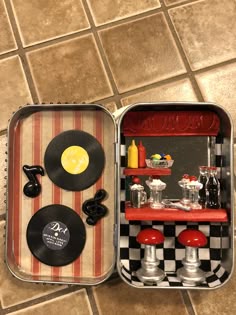 an open lunch box with various items in it on the floor next to a checkered tablecloth