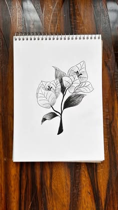 a spiral notebook with a drawing of flowers on the front and back cover, sitting on a wooden surface