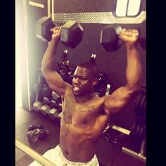 a shirtless man lifting two dumbbells in a room with other gym equipment