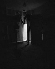 a person is standing in the dark with their arms out and there is an open door behind them