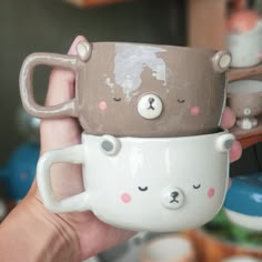 two coffee mugs with faces on them are being held by someone's hand