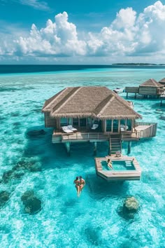 two people are swimming in the clear blue water next to some huts on stilts