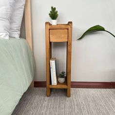 a small wooden shelf next to a bed with a plant on it and a book