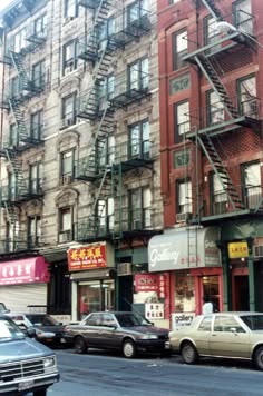 cars are parked on the street in front of tall buildings with fire escapes and balconies