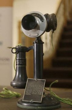an old fashioned camera on top of a wooden table next to a plaque and some green plants