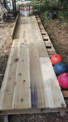 several bowling balls are lined up along the edge of a long wooden table that is being used as a bowling alley