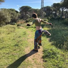 a woman walking down a dirt road next to grass and trees on a sunny day