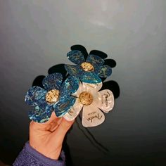 a person holding up some blue and white flowers with gold accents on their fingertipss