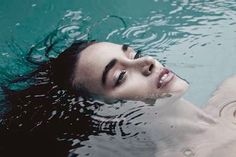 a woman is floating in the water with her eyes closed and head tilted to the side