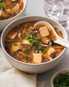 two bowls of soup with tofu and green onions in it, on a table