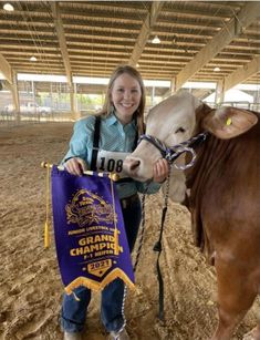 a woman is standing next to a cow holding a purple and yellow banner that says grand champion