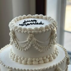 a three tiered white cake sitting on top of a table next to a window