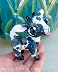 a hand holding a small figurine of a baby cow with big blue eyes