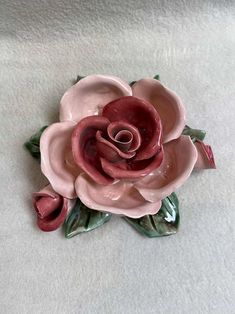 a pink flower with green leaves is on a white surface in the shape of a brooch