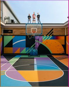 three people standing on top of a basketball hoop in front of a colorful painted wall