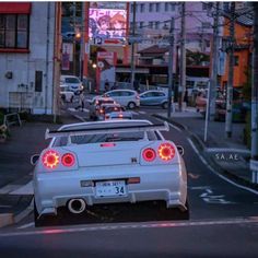 the back end of a white sports car on a city street at night with traffic lights