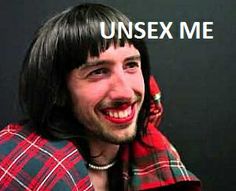 a man with long hair wearing a red and black plaid shirt smiles at the camera