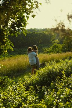 two people are walking through the grass with their arms around each other