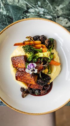 a white plate topped with meat and veggies on top of mashed potatoes