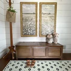 two framed pictures hang on the wall above a wooden bench with flowers in vases