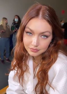 a woman with long red hair and blue eyes is looking at the camera while wearing a white shirt