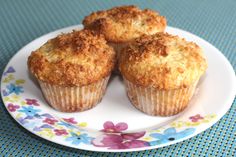 three muffins on a plate with flowers and blue table cloth in the background