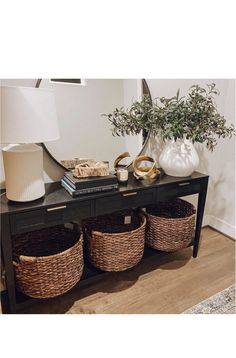 a black table with baskets on it and a lamp next to the end table in front of it