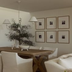 a dining room table with white chairs and pictures on the wall behind it, in front of a couch