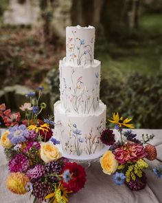 a three tiered white cake sitting on top of a table next to colorful flowers