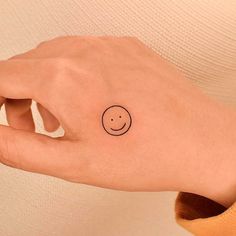 a person's hand with a smiley face tattoo on the left side of their wrist