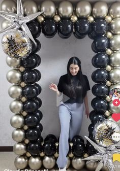 a woman standing in front of a black and silver balloon arch with stars on it