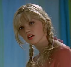 a blonde woman with braids on her hair looking off to the side in front of a blue curtain