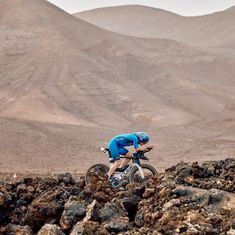 a man riding a bike on top of rocks in the desert with mountains in the background