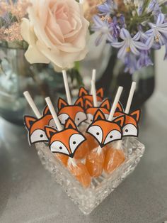 some lollipops are sitting in a glass bowl on a table next to flowers