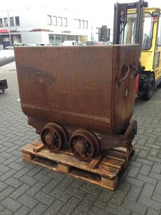 an old train cart sitting on top of a wooden pallet next to a yellow truck