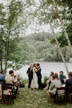 a bride and groom are kissing in front of the water at their outdoor wedding ceremony